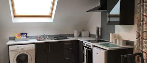A compact kitchen with a washing machine, a stove, a sink, and a window above the countertop.