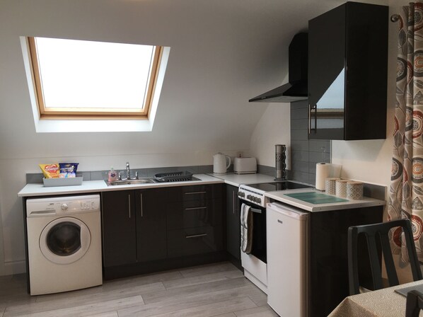 Cocina compacta con lavadora, estufa, lavaplatos y ventana sobre la encimera.