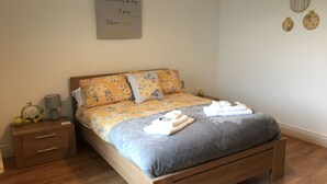A neatly made bed with floral bedding, a bedside table with a lamp, and a wall with a motivational quote. - Binnian View Apartment - Sleeps 4 (Newry)