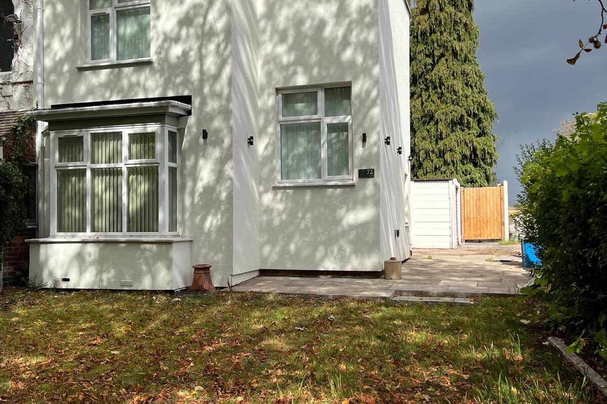 Een tweelaags huis met een witte gevel, een veranda en een houten omheining.