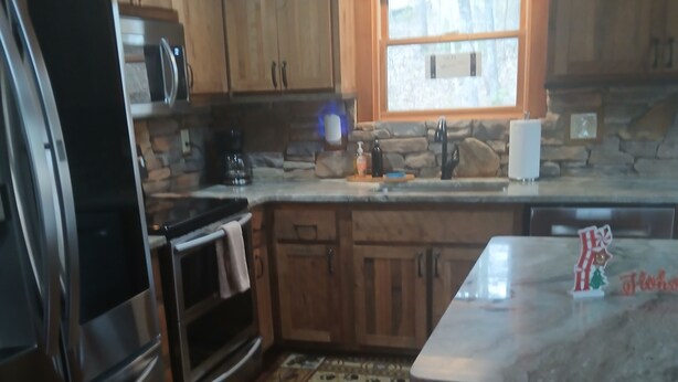 A kitchen with wooden cabinets, a stainless steel refrigerator, a microwave, and a stone fireplace. - Beautiful Cabin Perfect For Your Family Gathering in the North GA Mountains (Mineral Bluff)