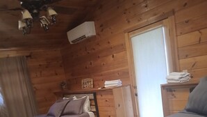 A wooden cabin room with two beds, a ceiling fan, a window, and a small table with towels. - Beautiful Cabin Perfect For Your Family Gathering in the North GA Mountains (Mineral Bluff)