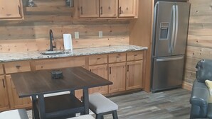 A kitchen with wooden cabinets, a stainless steel refrigerator, a marble countertop, and a dark wooden table with cushioned stools. - Beautiful Cabin Perfect For Your Family Gathering in the North GA Mountains (Mineral Bluff)