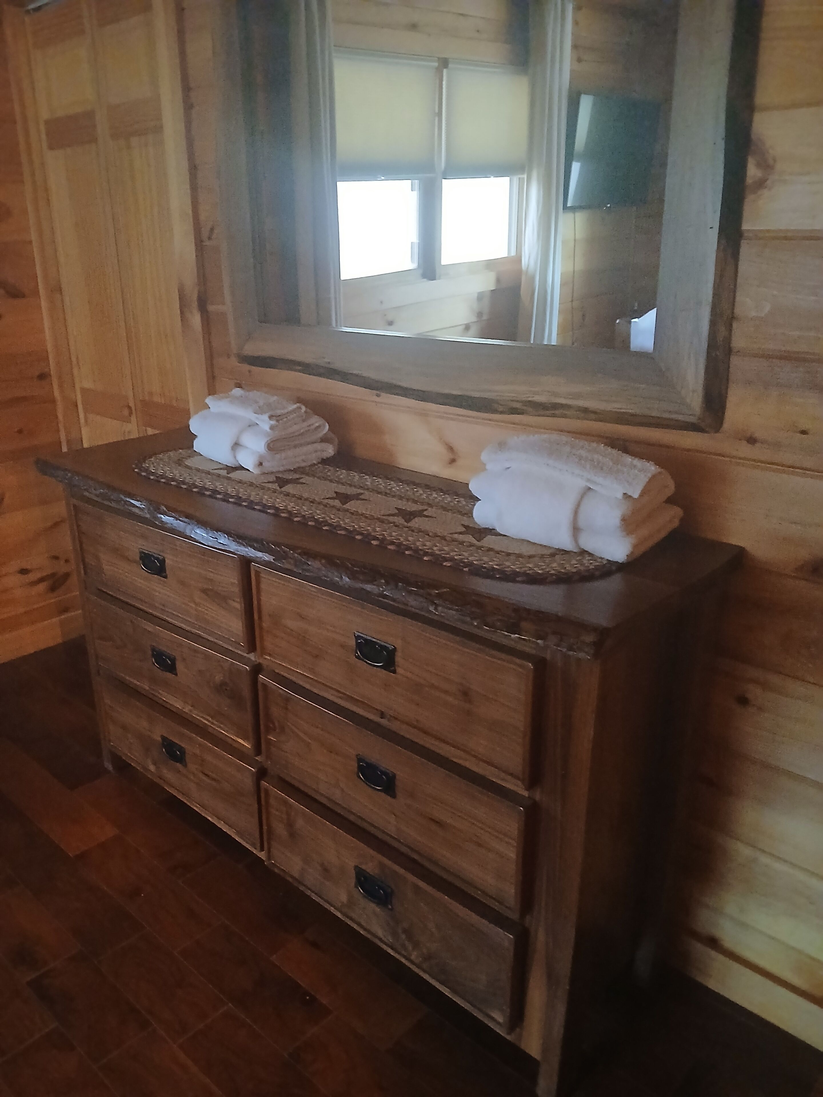 A wooden dresser with a mirror above it, and towels on top.