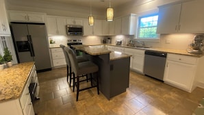 A modern kitchen with white cabinets, granite countertops, a central island with bar stools, a built-in oven, and a large window providing natural light. - Large Home with Entertainment Options Galore (Elizabethtown)