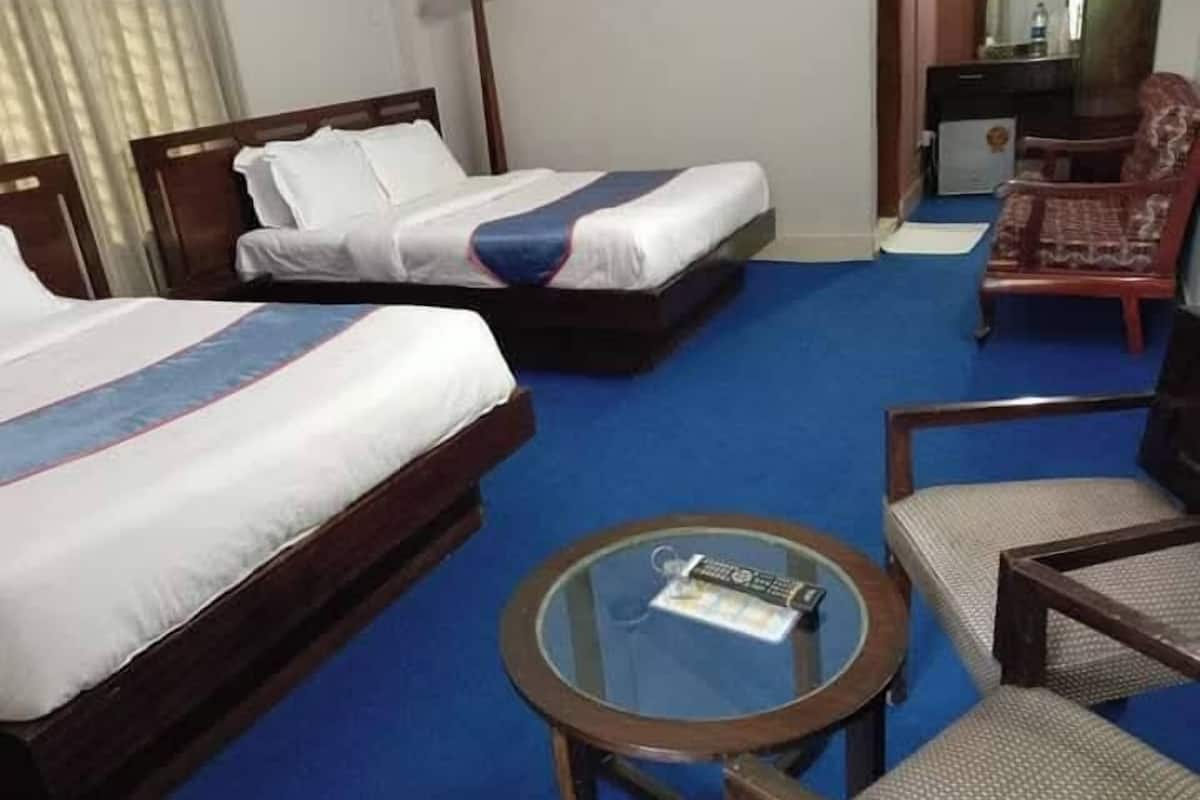 A hotel room with two beds, a small round table with a remote control, and a chair.