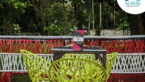 A table with a sign, surrounded by red and white lattice fencing, with greenery in the background. - Almas Hotel Sylhet  (Sylhet)