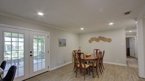 Un'area pranzo con un tavolo e sedie in legno, una porta bianca con pannelli di vetro e un elemento decorativo a parete.