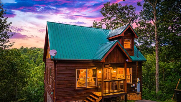 Eine Holzhütte mit grüner Dachdeckung, einer Veranda und einem Steinfundament.