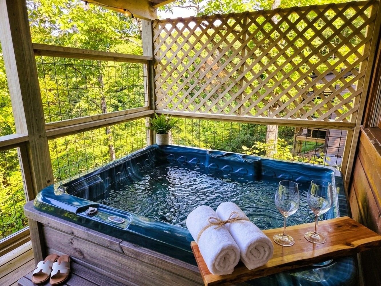 A hot tub with towels and glasses on a wooden deck, surrounded by a wooden fence and greenery.