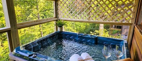 A hot tub with towels and glasses on a wooden deck, surrounded by a wooden fence and greenery.