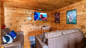 Ein gemütliches Blockhaus mit Holzwänden, einem Ledersofa, einem Fernseher und gerahmten Postern.