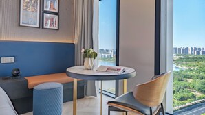 A modern hotel room with a large window, a round table, a bench, and framed pictures on the wall. - Chenfeng Hotel (Qingdao)