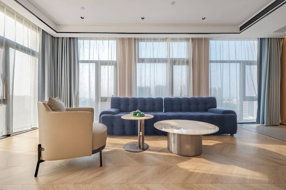Una sala moderna con un sofá azul, un sillón beige y una mesa de centro redonda.