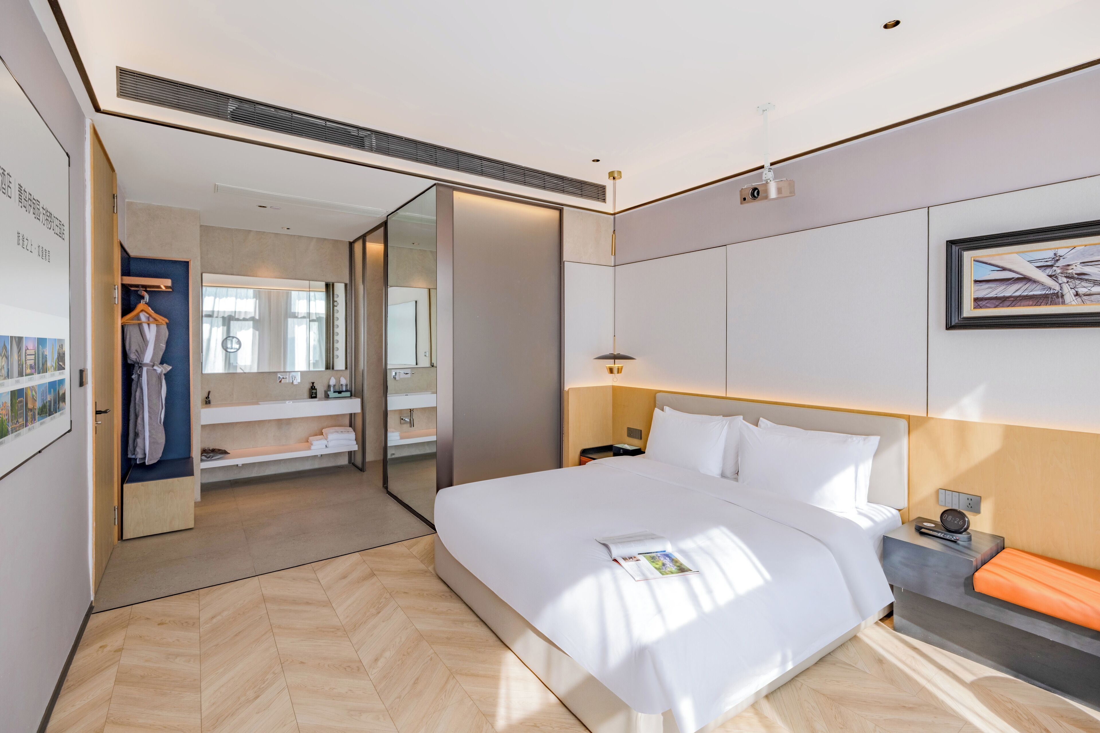 A modern hotel room with a large bed, a bedside table with a lamp, a mirror, and a view of the bathroom.