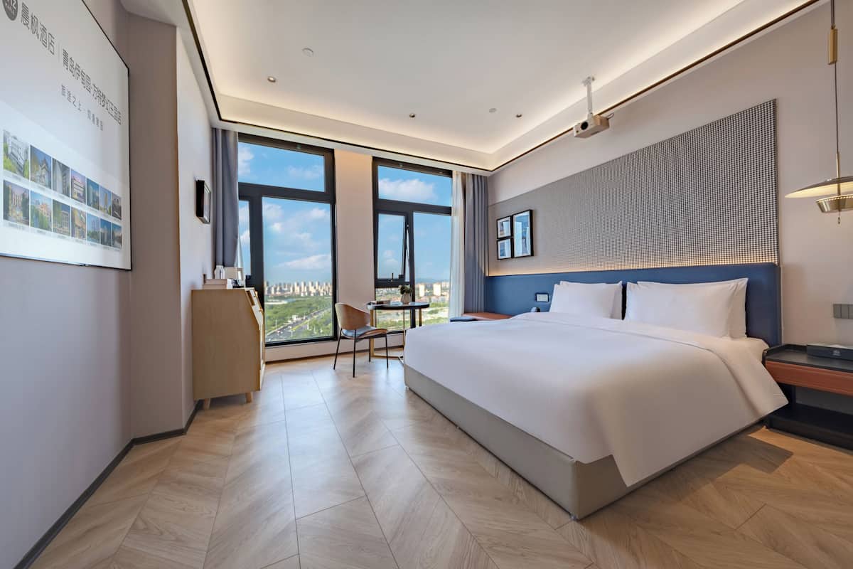 Habitación de hotel moderna con una cama grande, un escritorio y vistas de la ciudad a través de amplias ventanas.