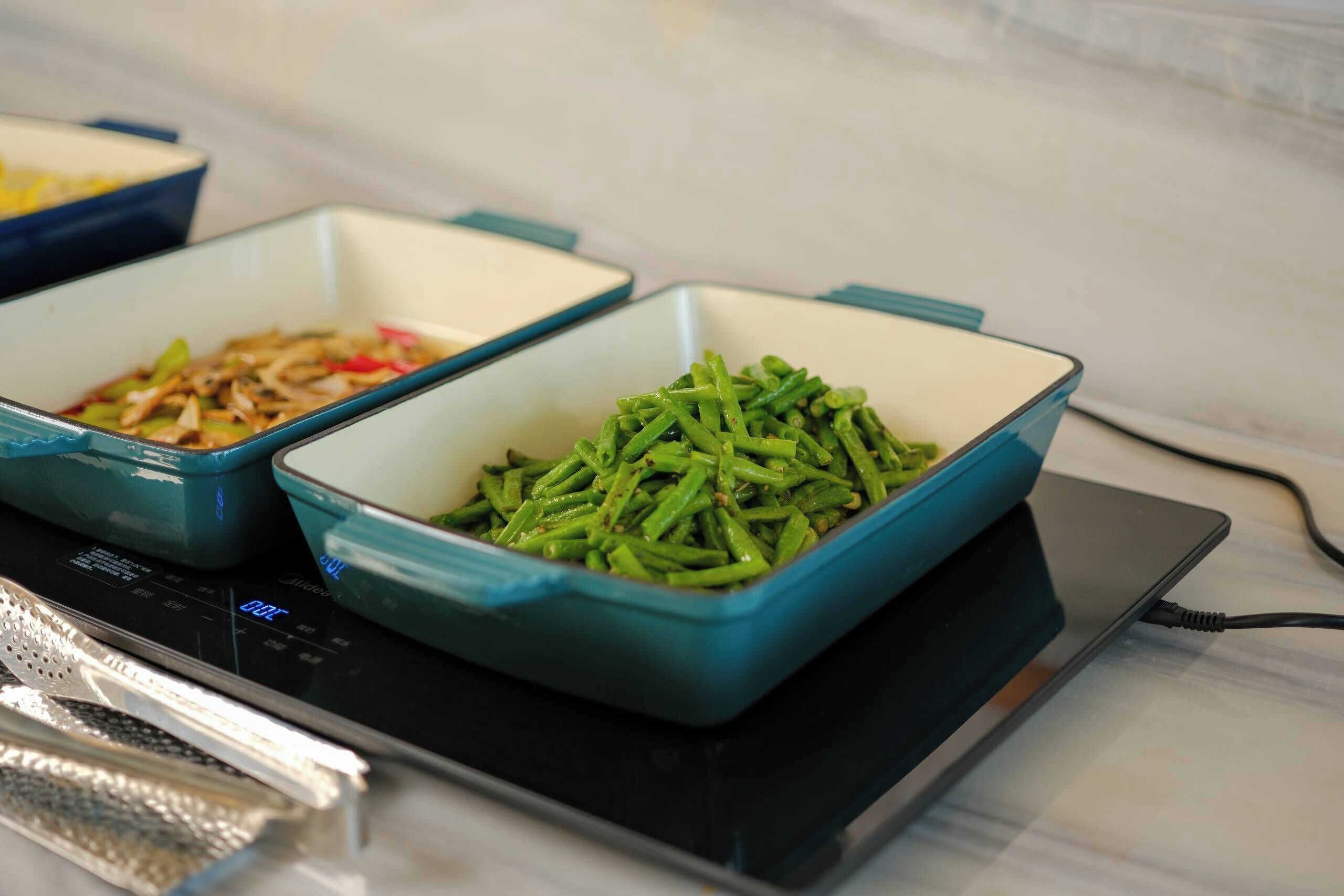 A kitchen with two blue bowls on an induction cooktop, one containing green beans and the other containing a different dish.