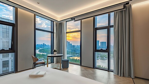 A modern hotel room with large windows, a bed, a small table, and a chair. - Chenfeng Hotel (Qingdao)