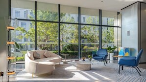 A modern lounge area with a sofa, chairs, and a coffee table, featuring large windows and a view of greenery outside. - Chenfeng Hotel (Qingdao)
