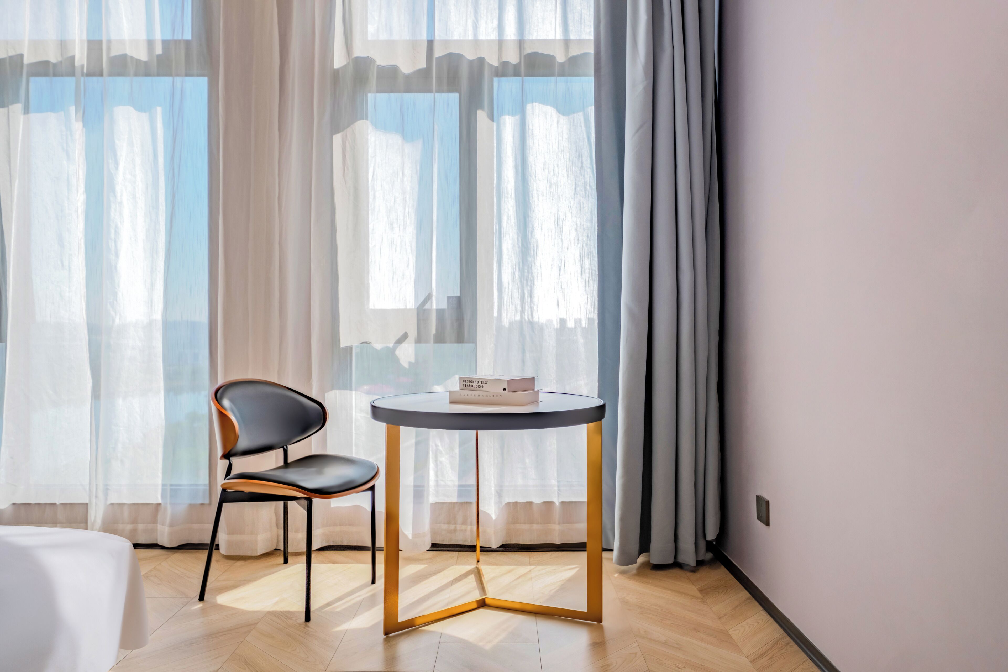 A modern room with a round table and a chair, a book on the table, and sheer curtains on the windows.
