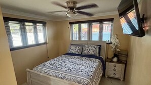 A bedroom with a bed, a nightstand, a ceiling fan, and a TV mounted on the wall. - Enjoyable 1-bedroom apartment with AC in welcoming Nassau (Nassau)
