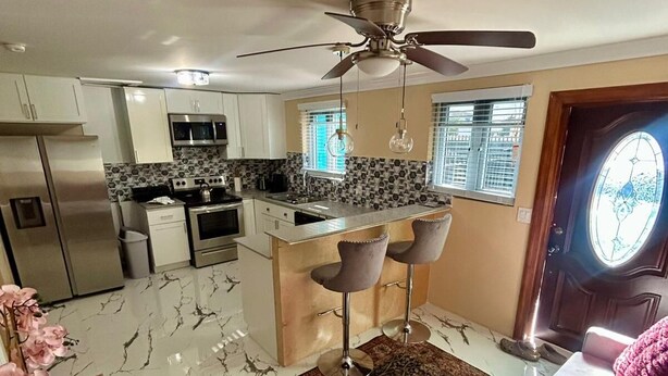 A modern kitchen with white cabinets, a central island, and a ceiling fan. - Enjoyable 1-bedroom apartment with AC in welcoming Nassau (Nassau)