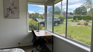 Quarto com uma janela grande, uma escrivaninha, uma cadeira e uma cama.