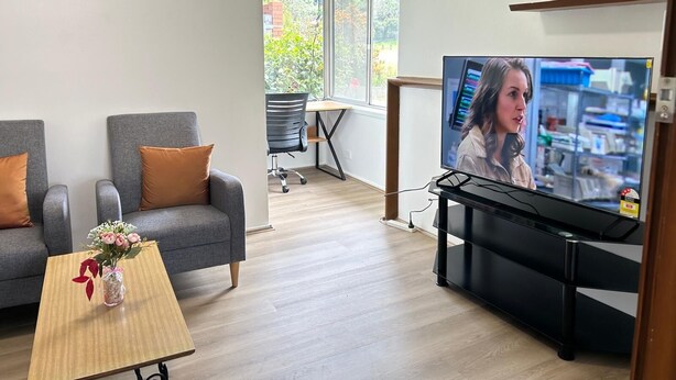 Uma sala de estar moderna com um sofá, uma mesa de centro com um vaso, uma televisão e uma escrivaninha com uma cadeira.