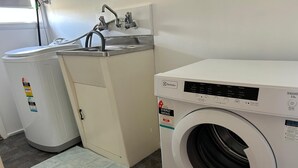 Uma área de lavanderia com máquina de lavar e secadora, pia e um tapete pequeno no chão.