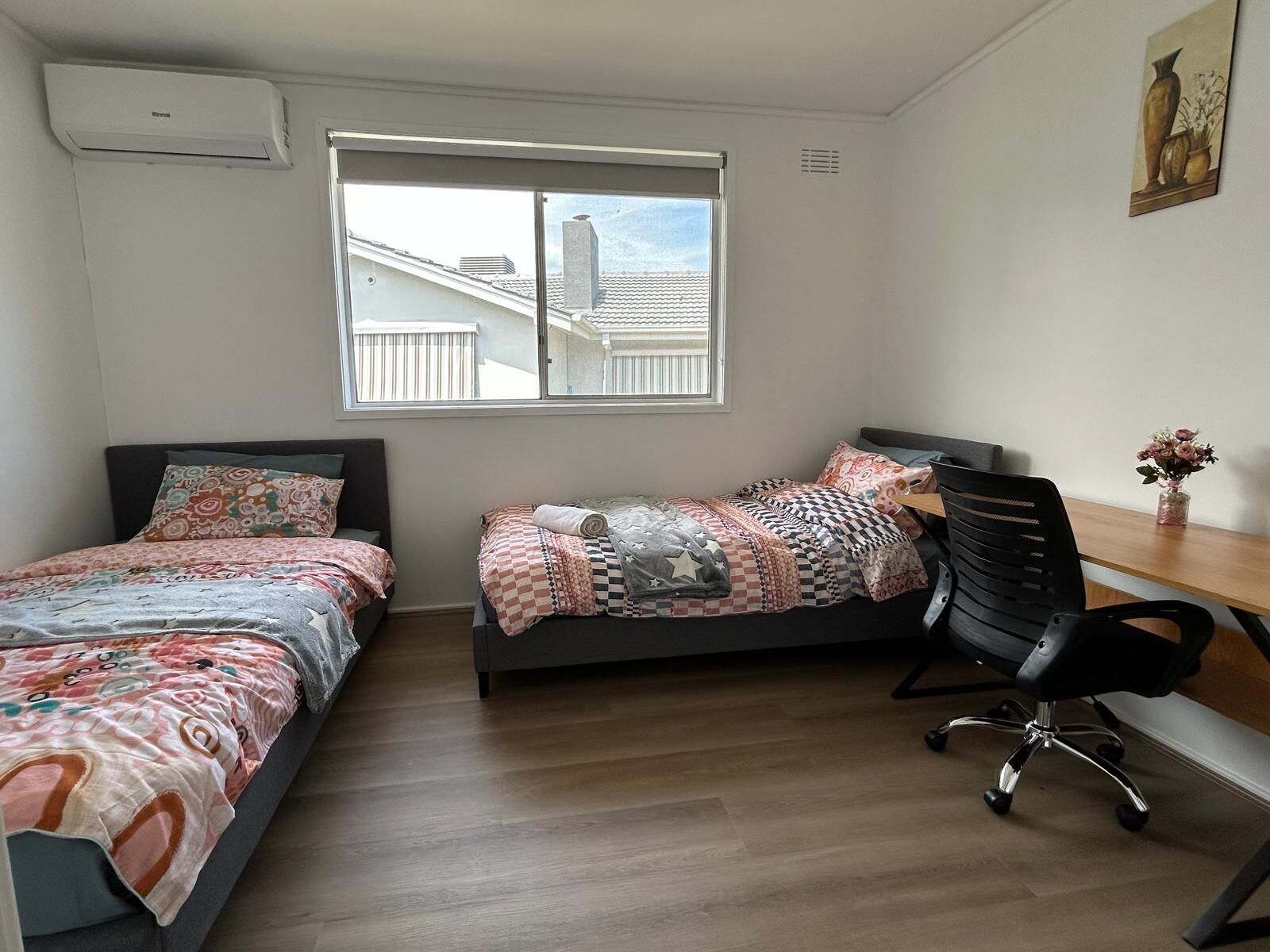 Un dormitorio con dos camas, un escritorio, una silla y una ventana con vista a edificios.