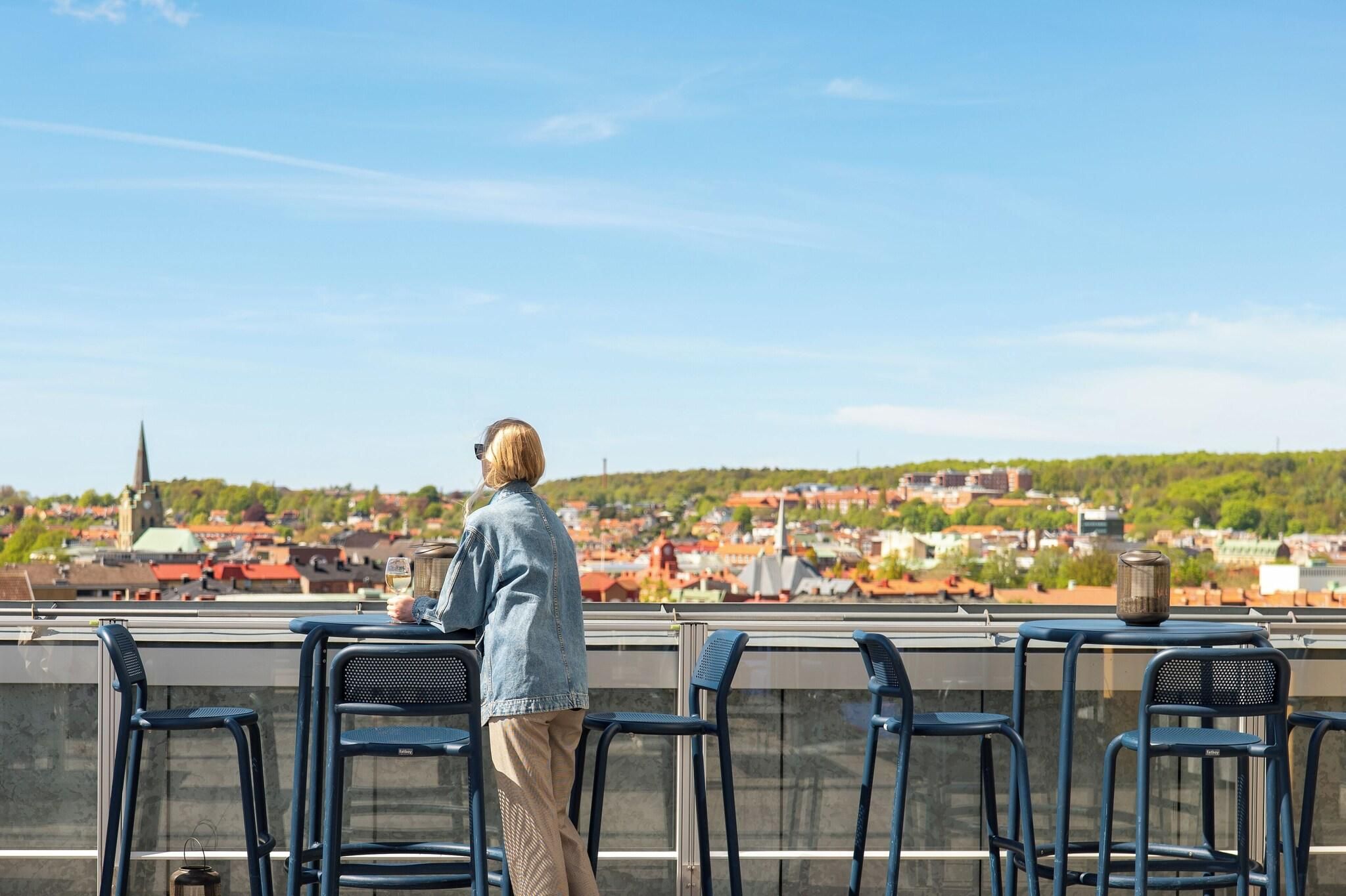 A person standing at a table with a view of a cityscape, including a church spire and residential buildings.