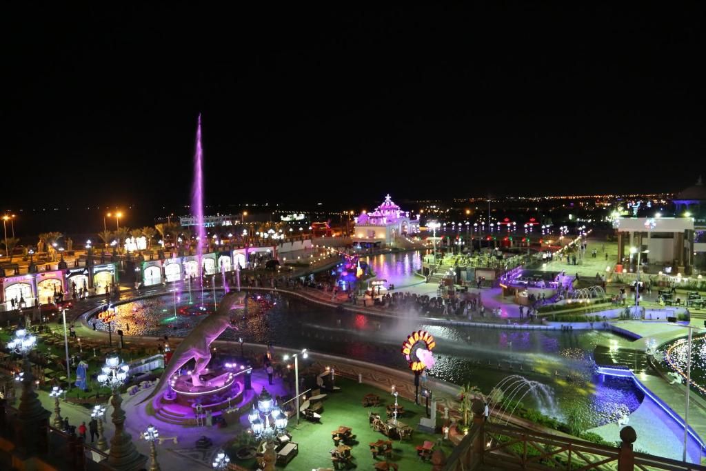 A nighttime view of a well-lit public square with a fountain, seating areas, and illuminated buildings.