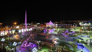 A nighttime view of a well-lit public square with a fountain, seating areas, and illuminated buildings.