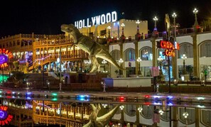 A nighttime view of a building with a large dinosaur statue in front, a 'Hollywood' sign, and a 'Chapel Cafe' sign. - Palma Di Sharm Resort (Sharm El Sheikh)