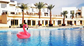 A swimming pool with a pink flamingo float, surrounded by a building with balconies and palm trees. - Palma Di Sharm Resort (Sharm El Sheikh)