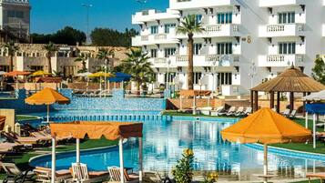Ett hotell med en swimmingpool, solstolar, parasoller och en byggnad med balkonger.