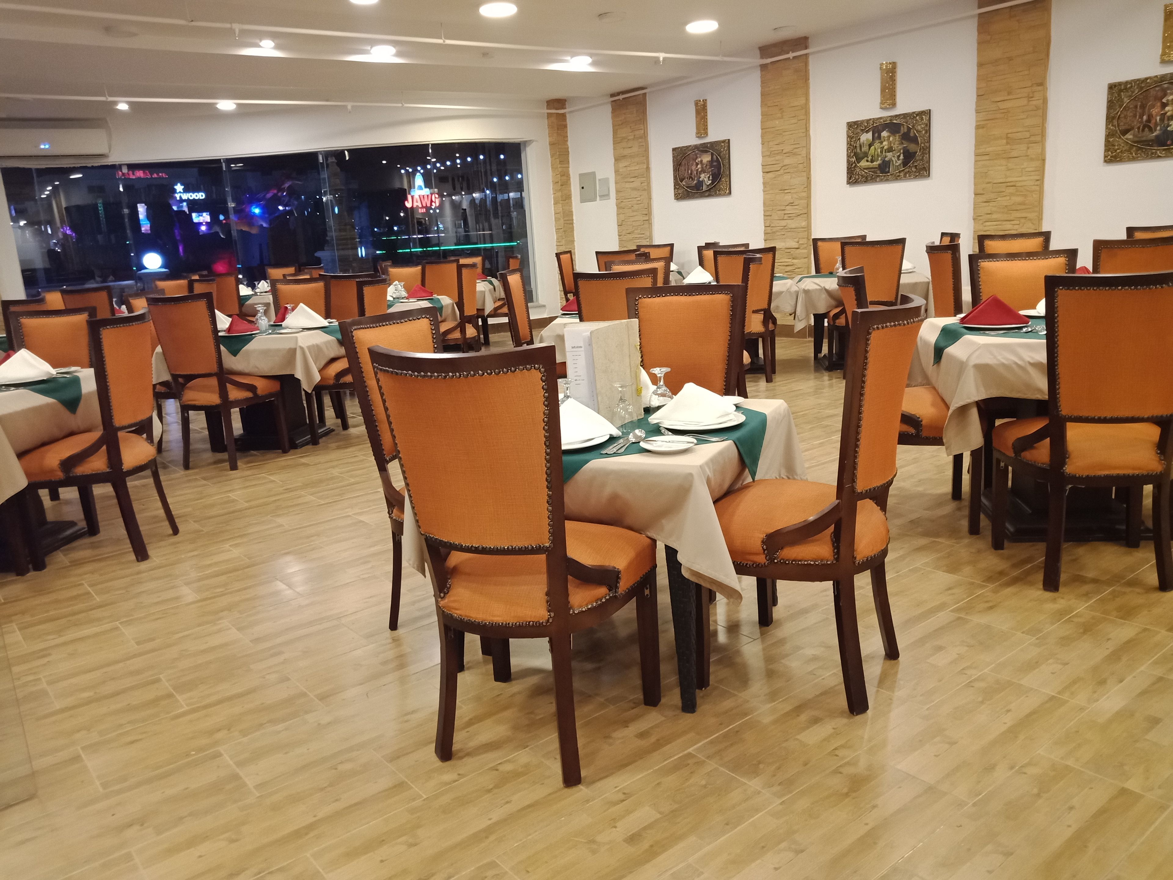 A restaurant with multiple tables and chairs, each set with white tablecloths and orange chairs.