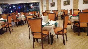 A restaurant with multiple tables and chairs, each set with white tablecloths and orange chairs.