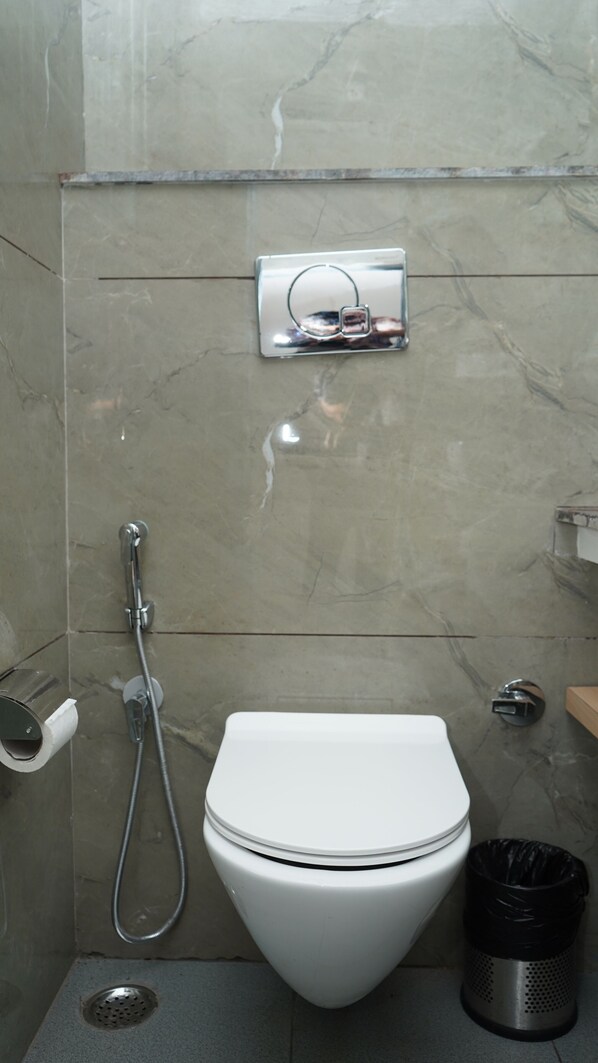 A modern bathroom with a white toilet, a shower, and a toilet paper holder. - The Whispering Winds Resort (Dehradun)