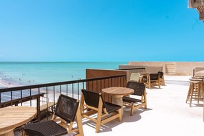 Une terrasse en bord de mer, avec des tables et des chaises en bois, offrant une vue sur l’océan.