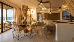 A spacious dining area with a round table and wicker chairs, a ceiling fan, and a view of the ocean. - Awa Holbox Hotel Boutique (Isla Holbox)