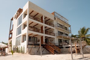 Un hôtel à plusieurs étages doté de balcons, d’un escalier et d’un sol sablonneux.