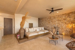 Una sala de estar moderna con una pared de piedra, un sofá, un ventilador de techo y plantas decorativas.