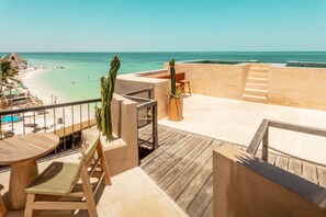 Une terrasse en bois avec une table et des chaises, donnant sur une plage et l’océan.