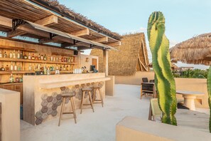 Ein Außenbereich mit Bar, einer Holztresore, Hockstühlen und einem Kaktus.