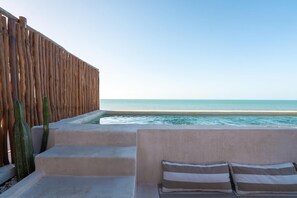 Une terrasse en bord de mer avec des marches menant à une piscine, une clôture en bois et un espace détente avec des coussins.