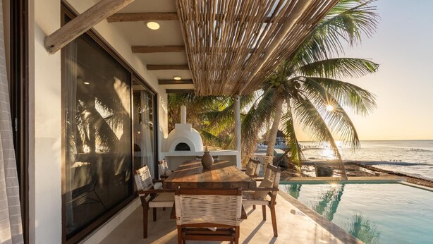 A patio with a wooden table and chairs, overlooking a pool and the ocean. - Awa Holbox Hotel Boutique (Isla Holbox)
