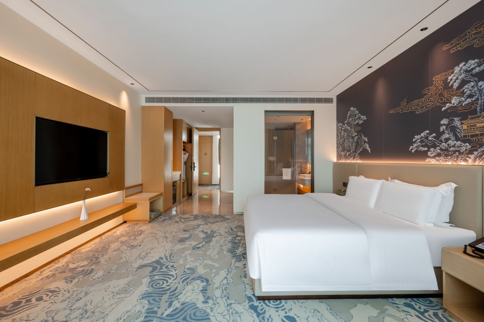 A modern hotel room with a large bed, a flat-screen TV mounted on the wall, and a decorative wall mural.