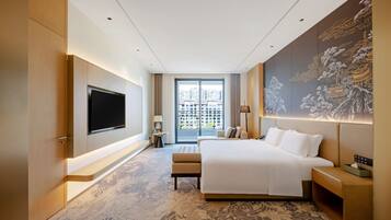 A modern hotel room with a large bed, a flat-screen TV, a large window with a city view, and a decorative wall mural.