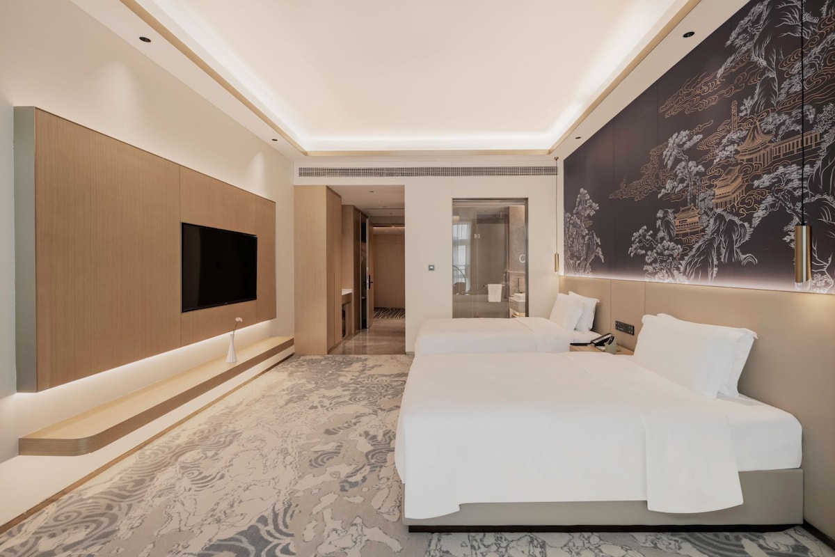 Une chambre d’hôtel moderne dotée d’un grand lit, d’un téléviseur à écran plat fixé au mur et d’une fresque décorative.